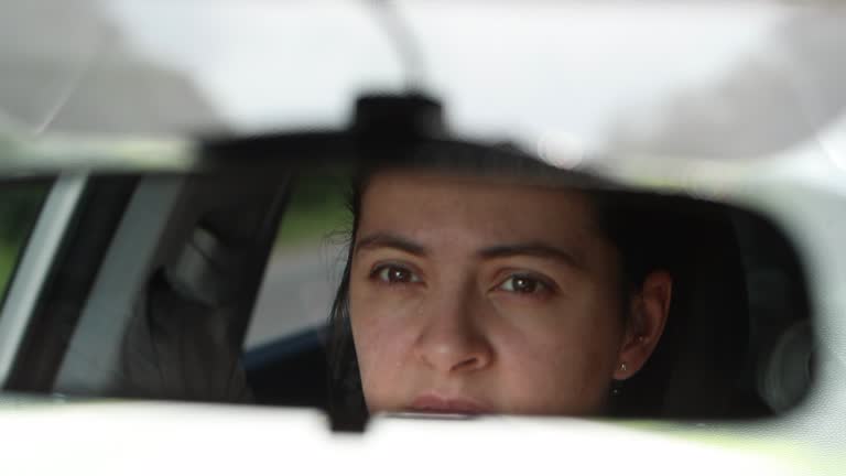 Driver checking rear-view mirror. Female driving on road reflected on mirror