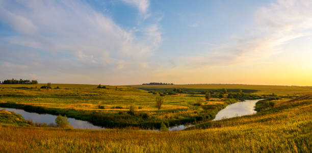 istock Sunny sunset view of river and green meadows with trees on a background. 1248086105