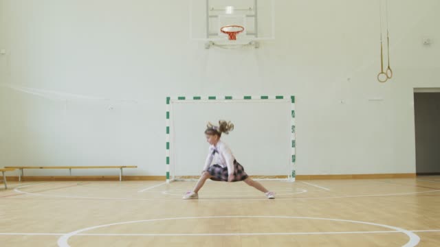 Little girl sits on the twine in the school gym. Girl performs gymnastic twine in the gym.