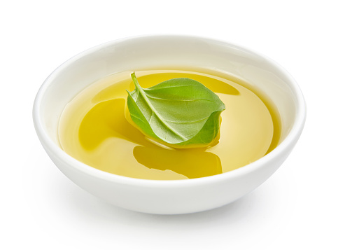 Olive or vegetable oil in white bowl. Oil with basil leaves isolated on white