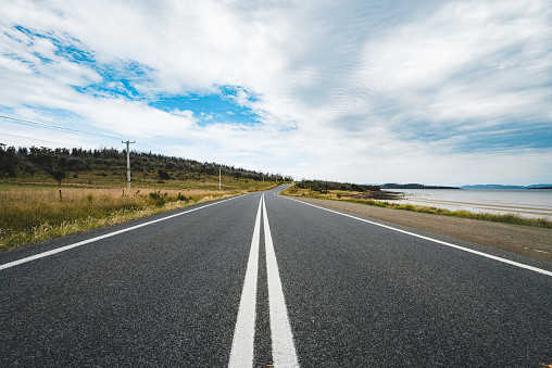 A long straight road without lines that crosses the Atacama desert in Chile. Sun with clouds in the blue sky.