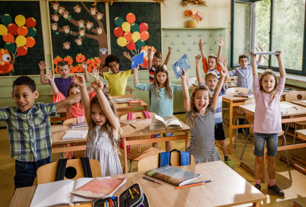 istock Large group of joyful elementary students with raised arms in the classroom. 1248119093