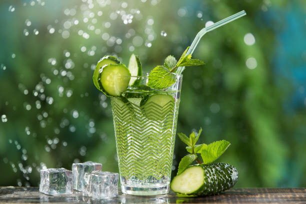 refreshing carbonated drink with ice and a straw, in a glass, next to cucumber and mint