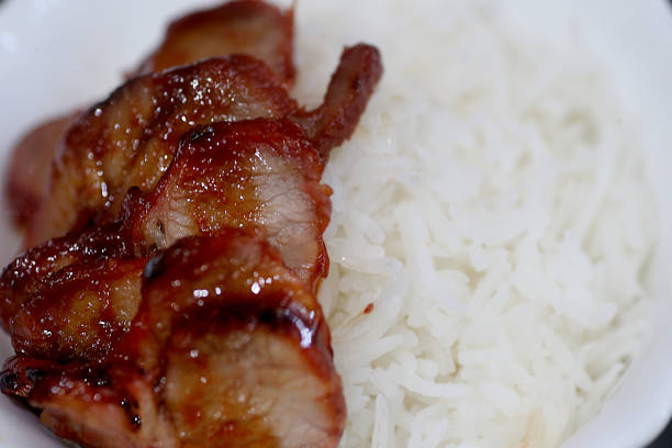 A focus scene on 'char siew' (barbeque pork) drizzle with sweet sauce on top of a bowl of steamed warm rice.