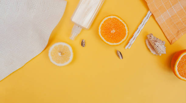 summer accessories hat, spray, shells, citrus fruits oranges, lemons and straw tubes on a bright yellow background. Sunny flatlay banner with space for text, top view