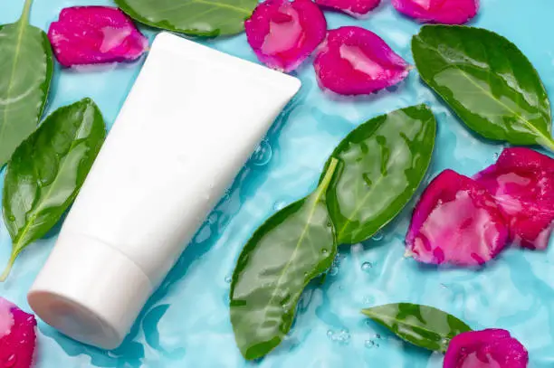Photo of White tube with cream against the background green leaves and rose petals in water