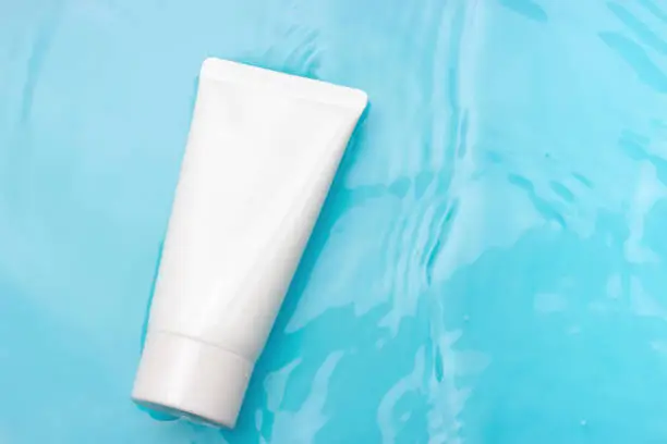 Photo of White tube with cream against the background of blue water, copy space