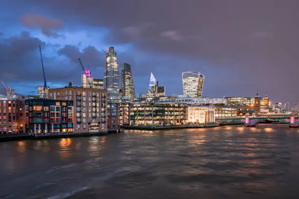 Panoramic high detail view towards London city's financial district iconic skyline during evening hours including all iconic downtown buildings with night illumination as photographed from the Thames Southbank river walk. Picture is ideal for background with extra copy space for financial and business concepts and ideas. Shot on Canon EOS R full frame system with premium RF lens for high quality and resolution.