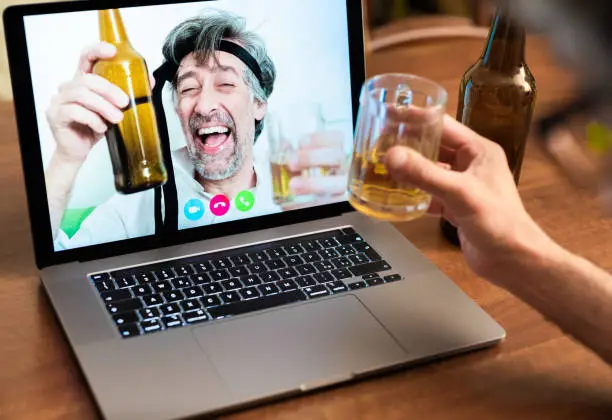 Work colleagues celebrate success by getting drunk on beers on long-distance video calls, friends lift their elbows during a video call