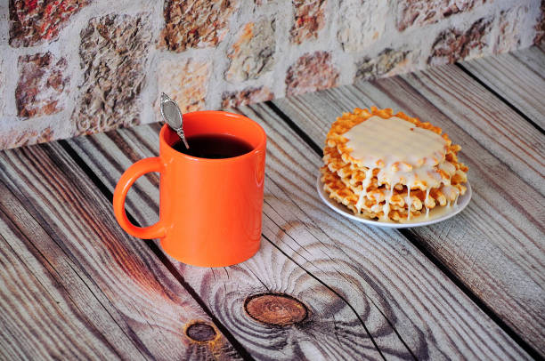 An orange mug of black coffee and a plate with flat waffles and white syrup.