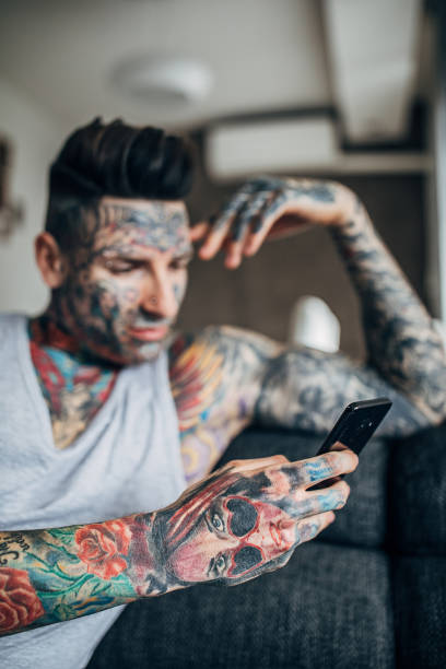 istock Young man with whole body covered in tattoos using smart phone at home 1248140533