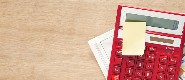 Red calculator with note and utility bills bill on wooden table with copy space