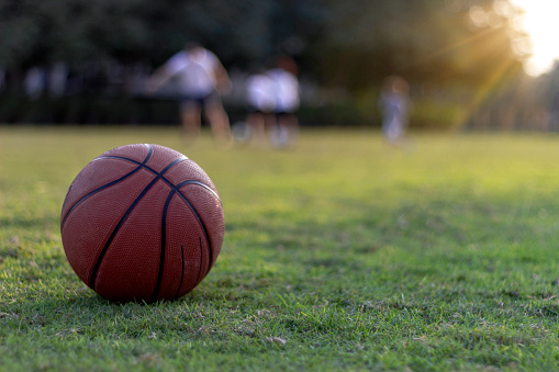 Silhouette action sport outdoors of group of kids having fun playing on green field.Basketball on grass field.Basketball on the green grass, background blurry image of group of people.Copy space.