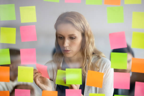 Businesswoman attaching to wall colorful sticky notes with tasks