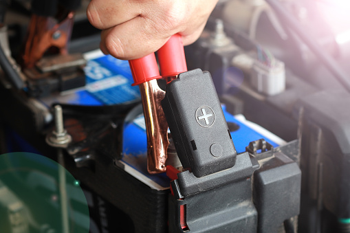 Close up of car battery anode cap with men's hand holding red electricity through cables for charging car