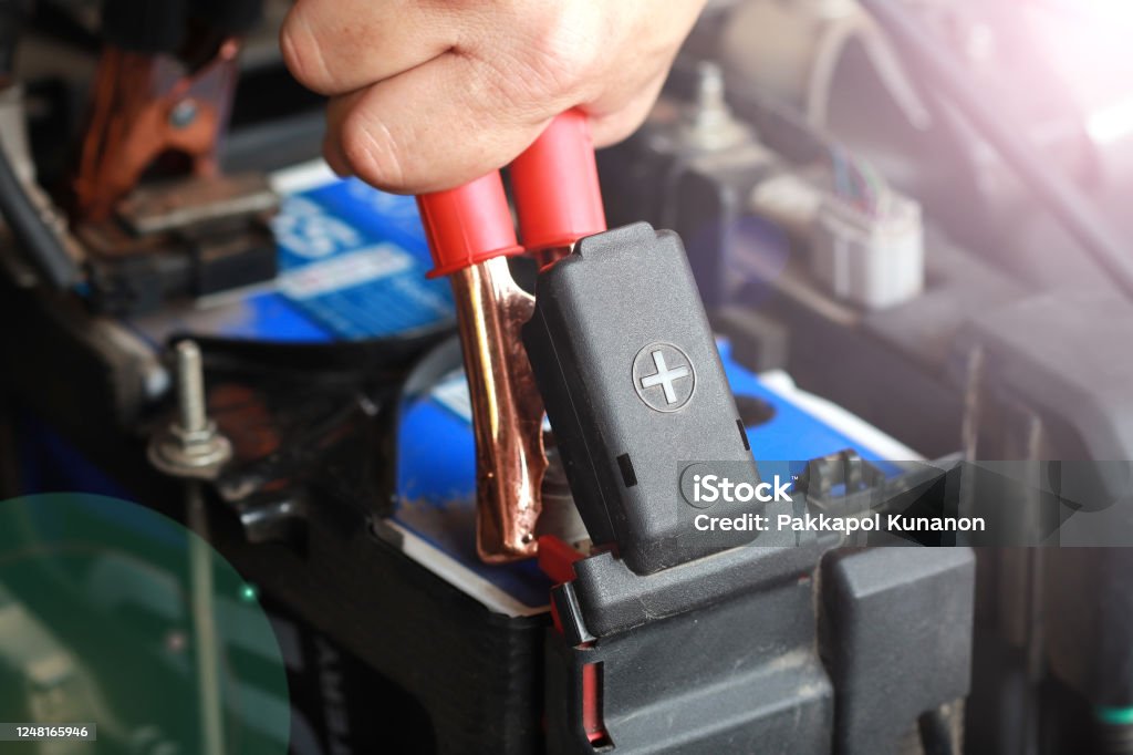 Car or vehicle preventive maintenance concept Close up of car battery anode cap with men's hand holding red electricity through cables for charging car Battery Charger Stock Photo