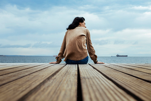 Back shot of a woman sitting on the edge of a seaside boardwalk