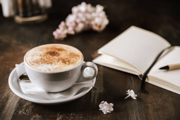 Cappuccino with cinnamon next to a lilac and a notebook. In a coffee shop on a dark table. selective focus.