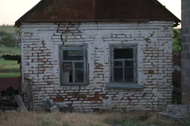 Photo of Facade of an old rural house with two windows. Abandoned building.