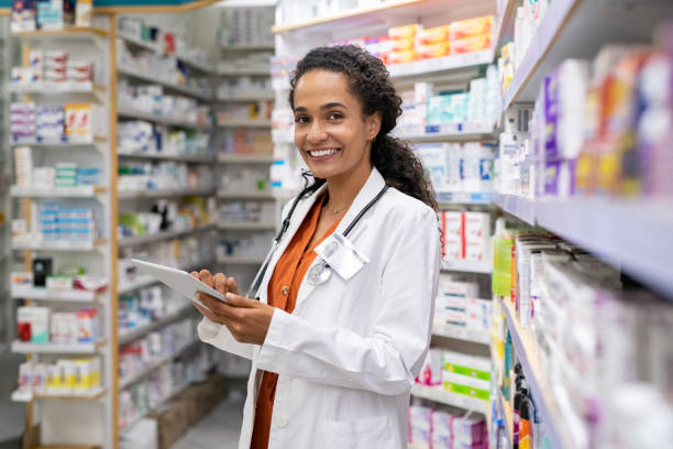 Young mixed race pharmacist using digital tablet Happy friendly multiethnic pharmacist doing inventory in a provided and modern pharmacy while looking at camera. Portrait of smiling young doctor woman working in drugstore with digital tablet. African smiling druggist working at hospital pharmacy. chemist stock pictures, royalty-free photos & images