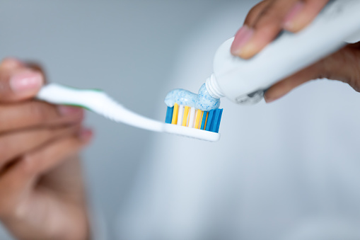 Close up African American woman applying toothpaste on toothbrush, holding in hands, girl squeezing dentifrice from plastic tube, personal oral hygiene and care, caries prevention, morning routine