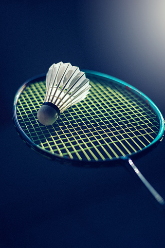 Image of Shuttlecock on badminton racket with spotlight and dark background.
