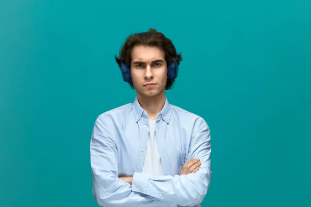I will not do it. Portrait of a young beautiful man wearing white t-shirt and blue shirt with headphones fold ones arms and looking at camera I will not do it. Portrait of a young beautiful man wearing white t-shirt and blue shirt with headphones fold ones arms and looking at camera over blue background. fur protest stock pictures, royalty-free photos & images