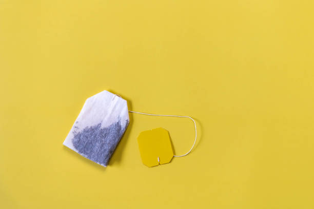 Tea bag with label on yellow background flat lay. Square green tea bag on yellow background with copy space. Teabag and yellow label. Wide banner with space for text on right side. Minimalism.