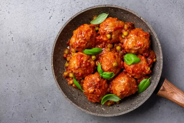 Turkey meatballs  in tomato sauce  with green peas and basil leaves.