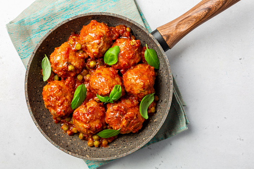 Turkey meatballs  in tomato sauce  with green peas and basil leaves. Flat lay, white background.