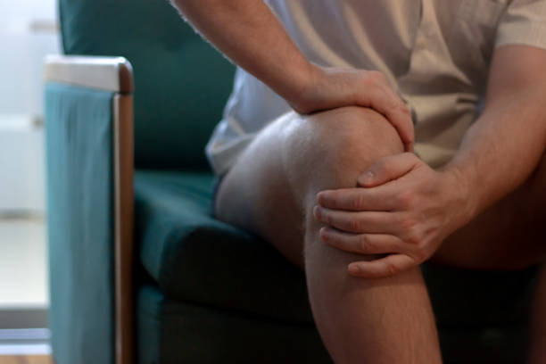 istock Mature man sitting on sofa touching his knee. 1248183476