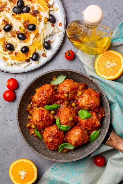 Mediterranian lunch. Turkey meatballs  in tomato sauce  with green peas, basil leaves and fennel salad with olives and oranges.