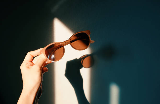 Mão mulher segurando óculos de sol da moda com sombra de luz solar com sombra na parede, conceito de moda e verão - foto de acervo