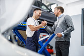 Happy auto mechanic and his manager greeting in a repair shop.