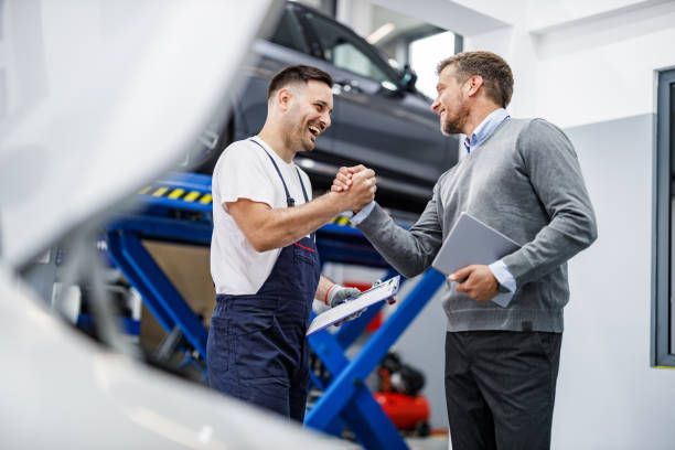 Happy auto mechanic and his manager greeting in a repair shop. Happy mechanic and his foreman greeting each other with a manly handshake in auto repair shop. auto repair shop stock pictures, royalty-free photos & images