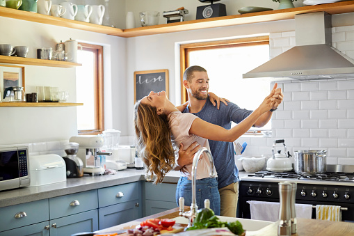 Happy man and woman dancing in kitchen. Romantic couple spending leisure time together. They are enjoying at home during lockdown.