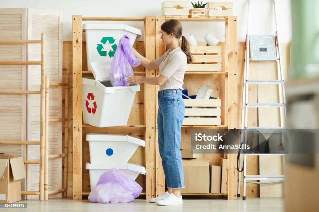 Woman sorting garbage into containers Young woman putting the package with garbage into the plastic containers she sorting the waste Garbage Bin Stock Photo