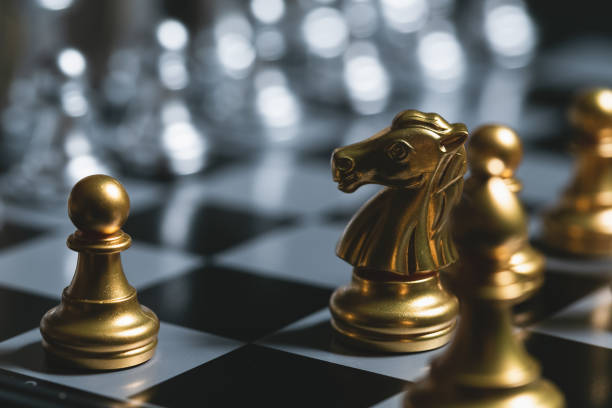 istock Gold pawn surrounded by gold chess pieces on a chess board. 1248200091