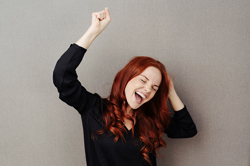 Motivated young woman cheering and celebrating a personal victory or win over a grey studio background