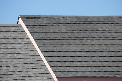 Roof shingles on top of the house against blue sky with cloud, dark asphalt tiles on the roof background.