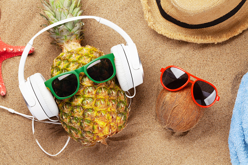 Ripe pineapple and coconut with sunglasses and headphones on hot sand beach. Travel and vacation concept. Top view flat lay