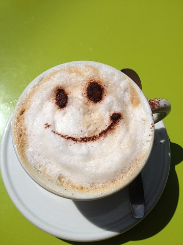 White coffee cup with Coffee with smiley face decoration on a lime green table