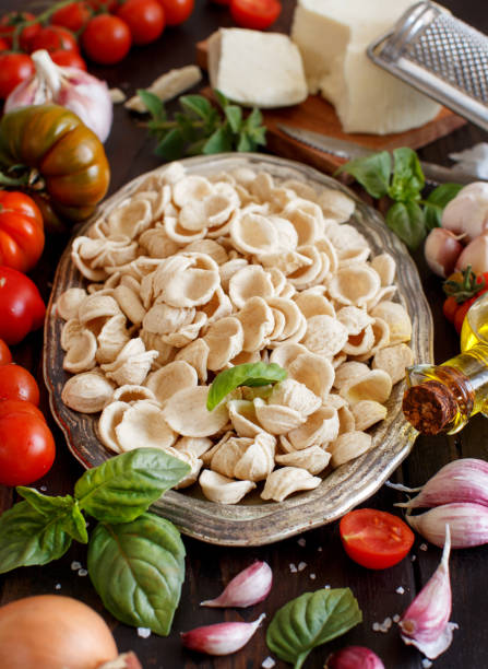 Fresh raw  italian pasta orecchiette, vegetables, herbs and olive oil Fresh raw italian pasta orecchiette on a tray, vegetables, herbs and olive oil close up, South Italian food concept puglia photos stock pictures, royalty-free photos & images