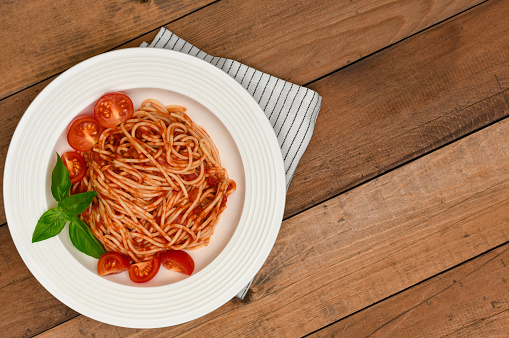 Plate of pasta with tomato sauce, basil and tomatoes Cherry on rustic background with copy space. Italian vegetarian spaghetti on wood background.