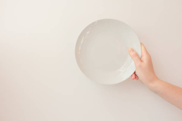 istock Female hand holds a white round plate on a white background as a mockup with copy space. Ceramic flat saucer 1248233015