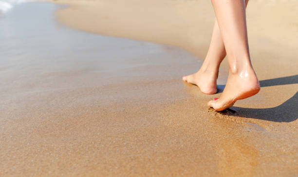 istock Female legs walk on the sea sand. 1248240619