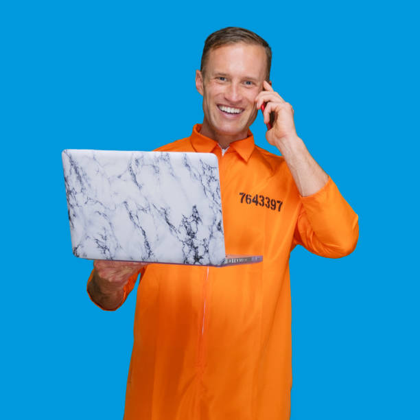 istock Criminal standing in front of blue background wearing jumpsuit and using laptop 1248243382