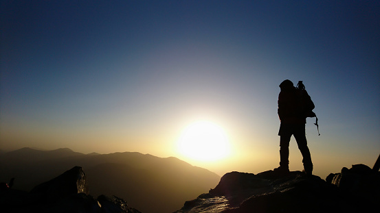Silhouette of a hiker watching a breathtaking sunrise from Toubkal peak, the highest in Atlas Mountains and North Africa. Morocco travel.