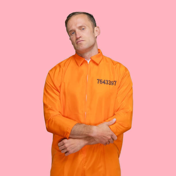 Criminal standing in front of colored background wearing uniform Portrait of criminal standing in front of colored background wearing uniform who is disappointed jumpsuit stock pictures, royalty-free photos & images