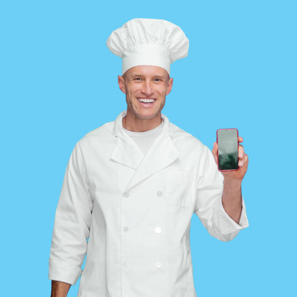 istock Caucasian young male chef standing in front of blue background wearing jacket and using mobile phone 1248247850